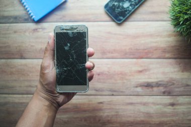 Bir insan ahşap bir yüzeyde çatlamış bir akıllı telefonu elinde tutar..