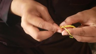 Bir insan parlak sarı iplik ve kanca kullanarak ustaca örgü örer..