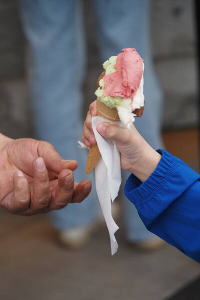 Ребенок охотно протягивает руку, чтобы ему предложили цветное мороженое..