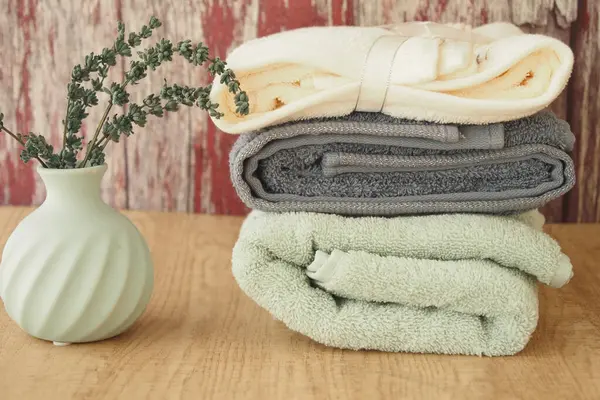 Yeşil vazolu basit bir vazonun yanına yeni katlanmış havlular..