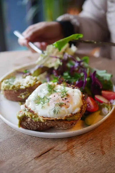 Yumurtayla kaplanmış taze avokado tostu. Tabakta renkli bir salata ile servis ediliyor..