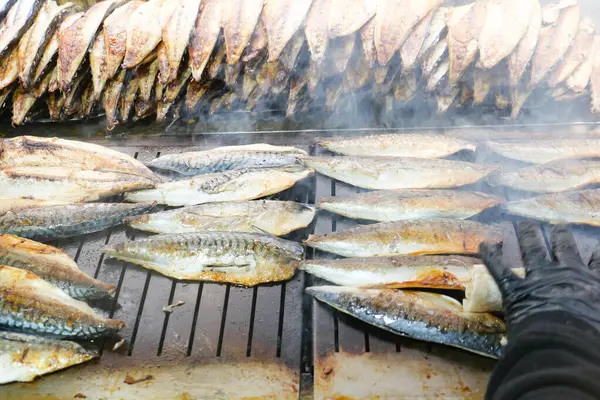 Bir şef güneşli bir günde açık hava pazarında uskumru pişirir..