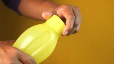 Eller parlak sarı bir şişenin kapağını bükerek içindekileri ortaya çıkarır..