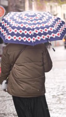 Bir insan yağmur altında renkli bir şemsiye altında şehir yolunda yürüyor..