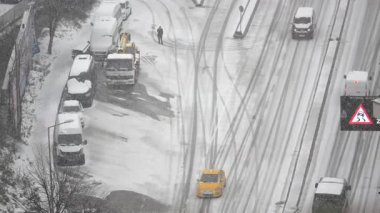 Şehir sokakları karla kaplı, araçlar duruyor ve sürücüler yolda..