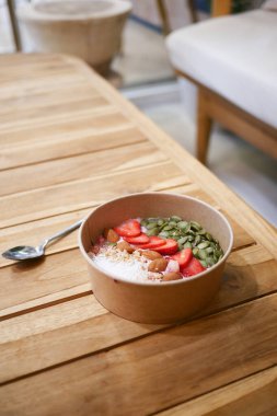 Besleyici bir kahvaltı kasesi, üzerinde çilekler olan ahşap bir masada oturur..