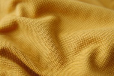 Yumuşak dalgaları ve kıvrımları gösteren desenli sarı kumaşın yakın görüntüsü.