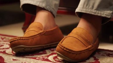 Sıcak bir halıda otururken rahat bir mokasen giyerek rahatlayan bir insan..