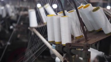 Meşgul tekstil fabrikasında beyaz iplik makaraları asılı..