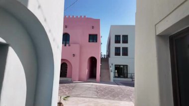 Açık bir avluda açık mavi gökyüzünün altında parlak pastel binalar duruyor..