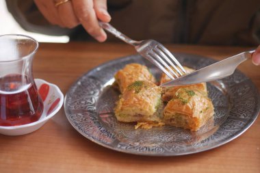 Bir insan çay içerken taze pişmiş baklavanın tadını çıkarıyor..