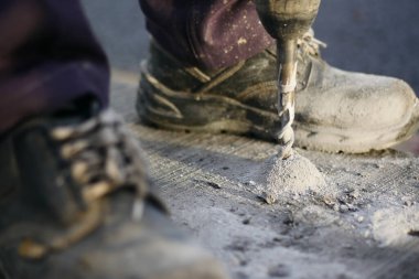 Bir işçi güvenlik ayakkabısı giyerken beton matkap kullanır..