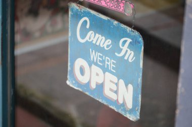 Parlak mavi tabela bir dükkan vitrininde asılı, ziyaretçileri içeri alıyor..