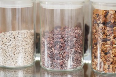 Tohumlarla dolu üç cam kavanoz, kakao parçaları ve granola karışımı..