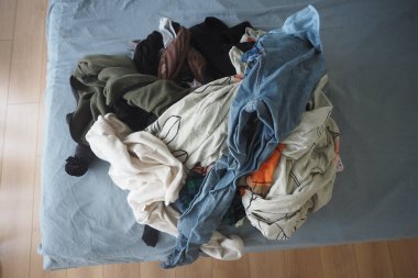 Renkli giysiler bir yatakta üst üste yığılır, düzenlenmeye ve bakıma ihtiyaç duyarlar..