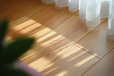 Güneş ışığı perdelerin arasından süzülür ve yerde hassas gölgeler yaratır..