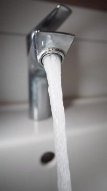 Pürüzsüz bir musluktan beyaz bir lavabo havzasına temiz su akıntıları.