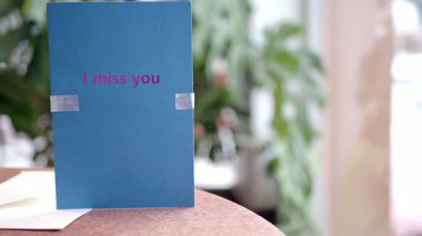 Seni özlediğim kelimelerin yazılı olduğu mavi bir kart. Bir masada sergilenmiş, davetkar bir bağlantı..