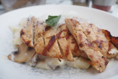 Mantarlı ve otlu kremalı makarna üzerinde sulu ızgara tavuk dilimleri..