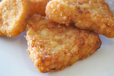 Kızarmış tavuk parçaları beyaz bir tabakta, çıtır çıtır dokularını sergiliyorlar..