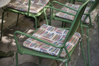 Benzersiz minderleri olan parlak renkli sandalyeler dışarıda güneşin altında otururlar..