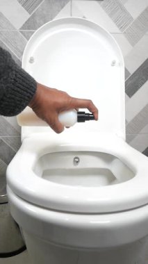 Kişi tuvalet temizliği ve tazeliğini korumak için temizleyici kullanır..