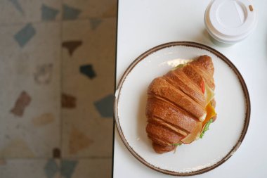 Lezzetli bir kruvasan tabakta bir içeceğin yanında duruyor..