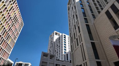 Kalabalık bir kentsel alanda mavi gökyüzüne karşı yüksek binalar yükselir..