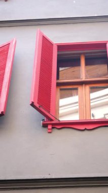 Kırmızı panjurlar gri duvara çarpıyor, pencereyi vurguluyor..