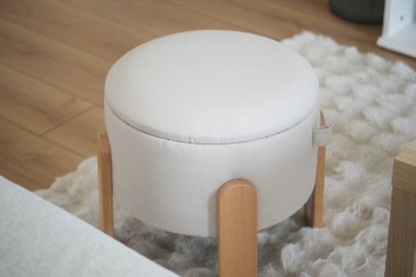 Konforlu bir oturma odasında ahşap bacaklı, modern, yuvarlak bir şilte bulunur..