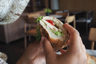 Bir insan taze yapılmış bir sandviçi marul ve domatesle tutuyor..