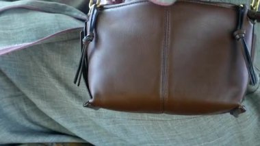 Kahverengi deri bir çanta tutan kadın.,