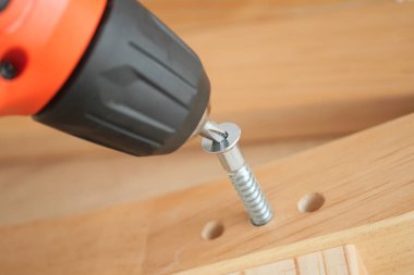 Elektrikli bir alet, metal bir vidayı tahta bir yüzeye sokuyor..
