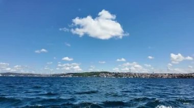 Sakin su, kıyı şeridine yakın beyaz bulutlu mavi bir gökyüzünü yansıtır..