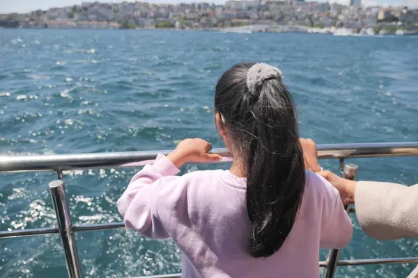 Çocuk teknede dolaşırken suya ve şehir manzarasına bakıyor..