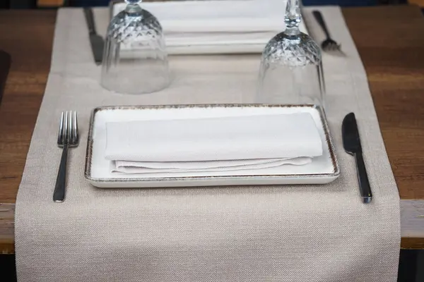 Güzel düzenlenmiş bir yemek masasında beyaz tabaklar ve kristal bardaklar sergileniyor..