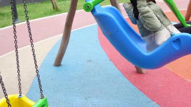 Bir çocuk güneşli bir günde renkli bir oyun alanında neşeyle sallanır..