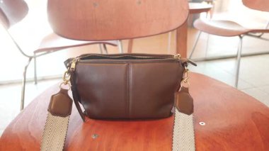 Kahverengi bir çanta, rahat bir kafede, ahşap bir sandalyede duruyor..