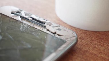 Kırık bir akıllı telefon bir fincan kahvenin yanındaki masada duruyor..