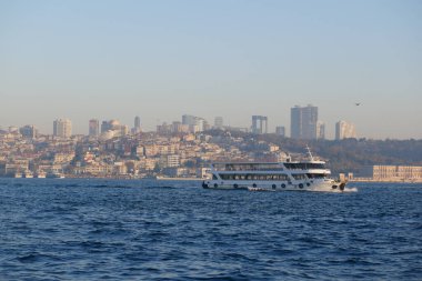Bir feribot, alacakaranlıkta şehrin önündeki ufuk çizgisinde hareket eder..