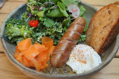 İçinde sosis, yeşillik ve taze sebzeler bulunan renkli bir kahvaltı kasesi..