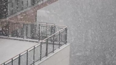 Sakin bir kentsel alandaki binaları ve balkonları bir kar yağışı kaplıyor.