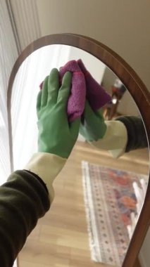 Eldiven ve bez kullanarak aynayı nasıl temizleyeceğini gösteriyor..