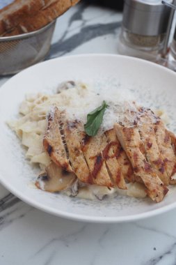 Izgara tavuk fettuccine 'in üzerinde dinleniyor, otlar ve peynirle süslenmiş..