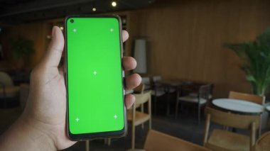 Yoğun bir kafe ortamında yeşil ekranlı bir akıllı telefon görüntüler.
