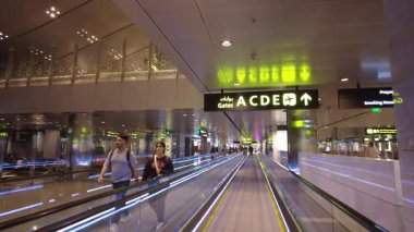 İnsanlar hareket halindeki bir geçitten uçuş kapılarına doğru yürüyorlar..