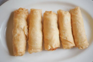 Dört mükemmel kızarmış börek beyaz bir tabakta düzgünce dizilmiş..