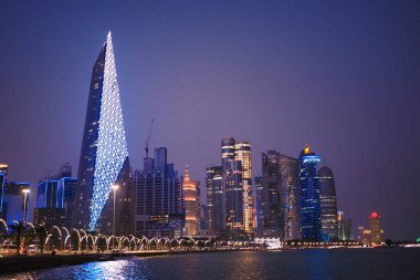 Parlak gökdelenler günbatımında modern bir şehrin sularını yansıtıyor..