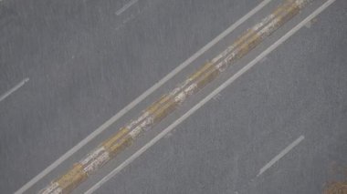 Şehir sokaklarına sürekli yağmur yağıyor, ıslak yüzeyler ve su birikintileri yaratıyor..