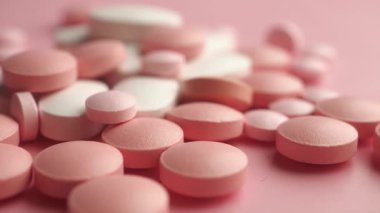 Pembe arka plana yayılmış pembe ve beyaz haplardan oluşan bir derleme..